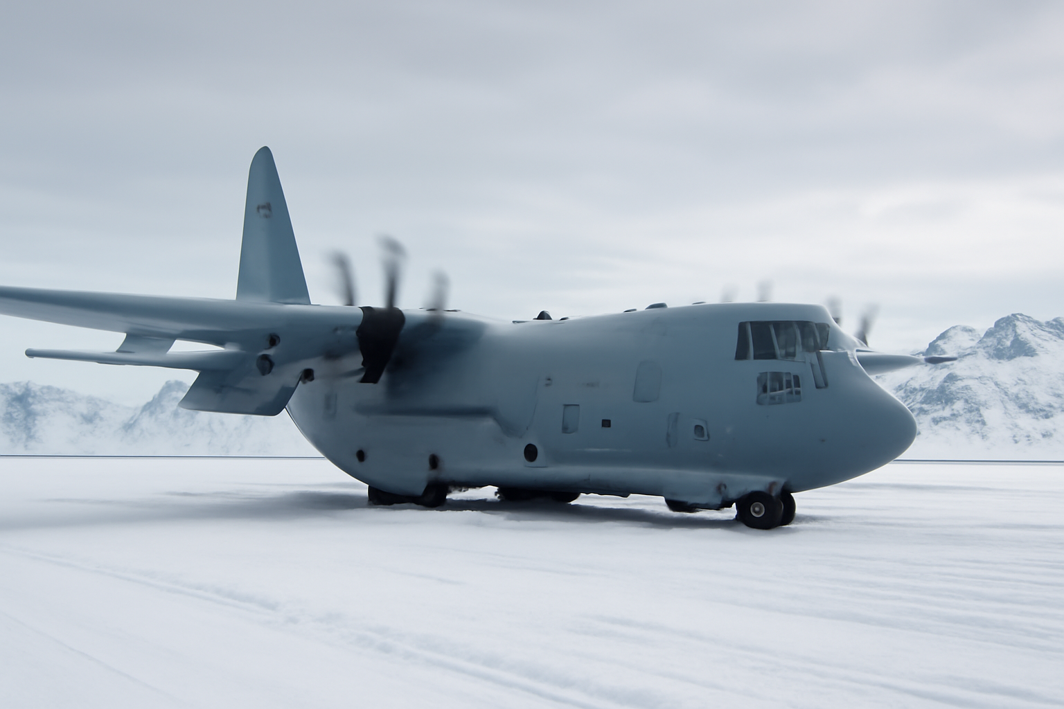 Military aircraft on a snow-covered airfield in Greenland with mountains in the background