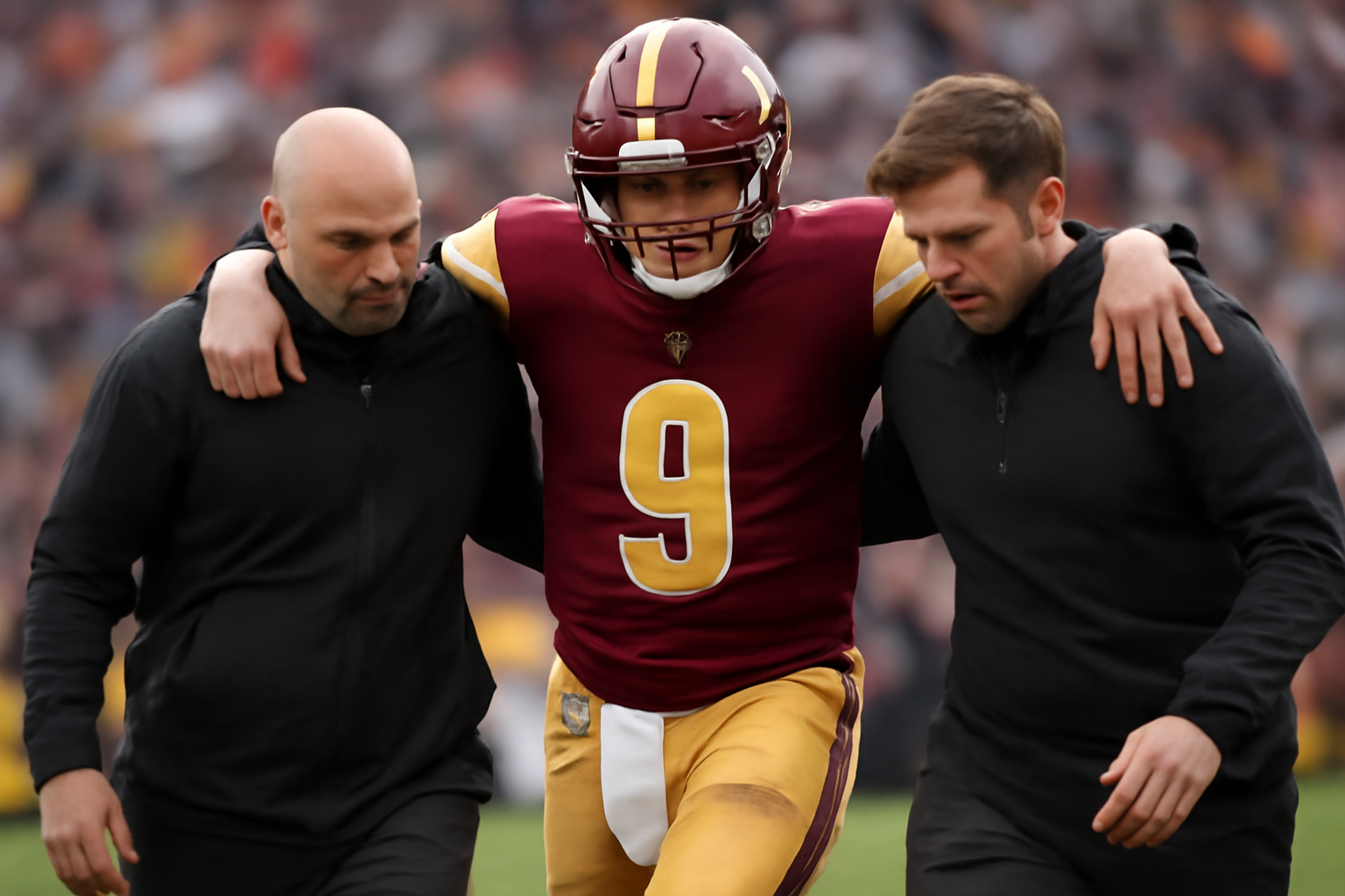 A quarterback in a burgundy and gold uniform being helped off an NFL field by medical staff