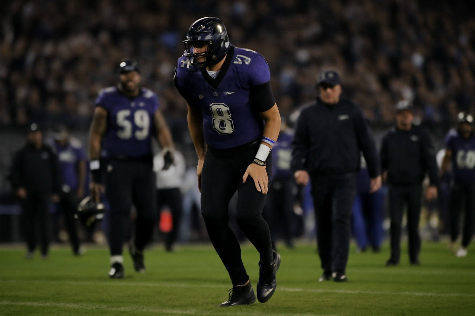 An NFL quarterback in a dark purple jersey walking toward the sideline with a visible limp during a game