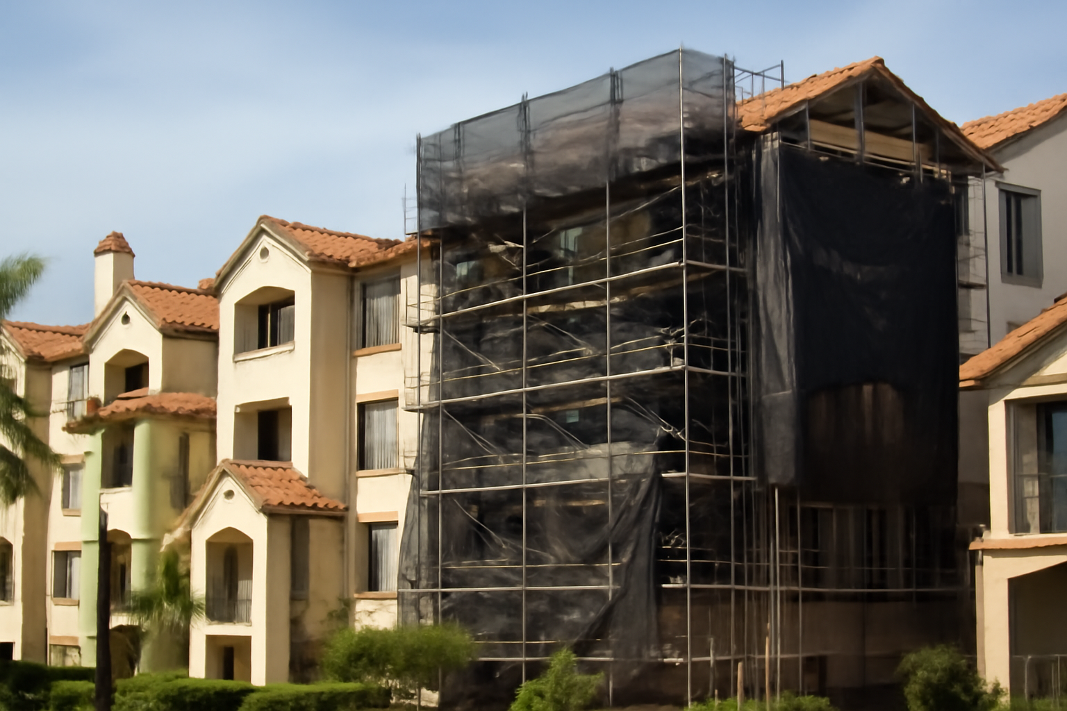 Rows of beige condominium buildings with tile roofs under repair scaffolding in a Southern California complex