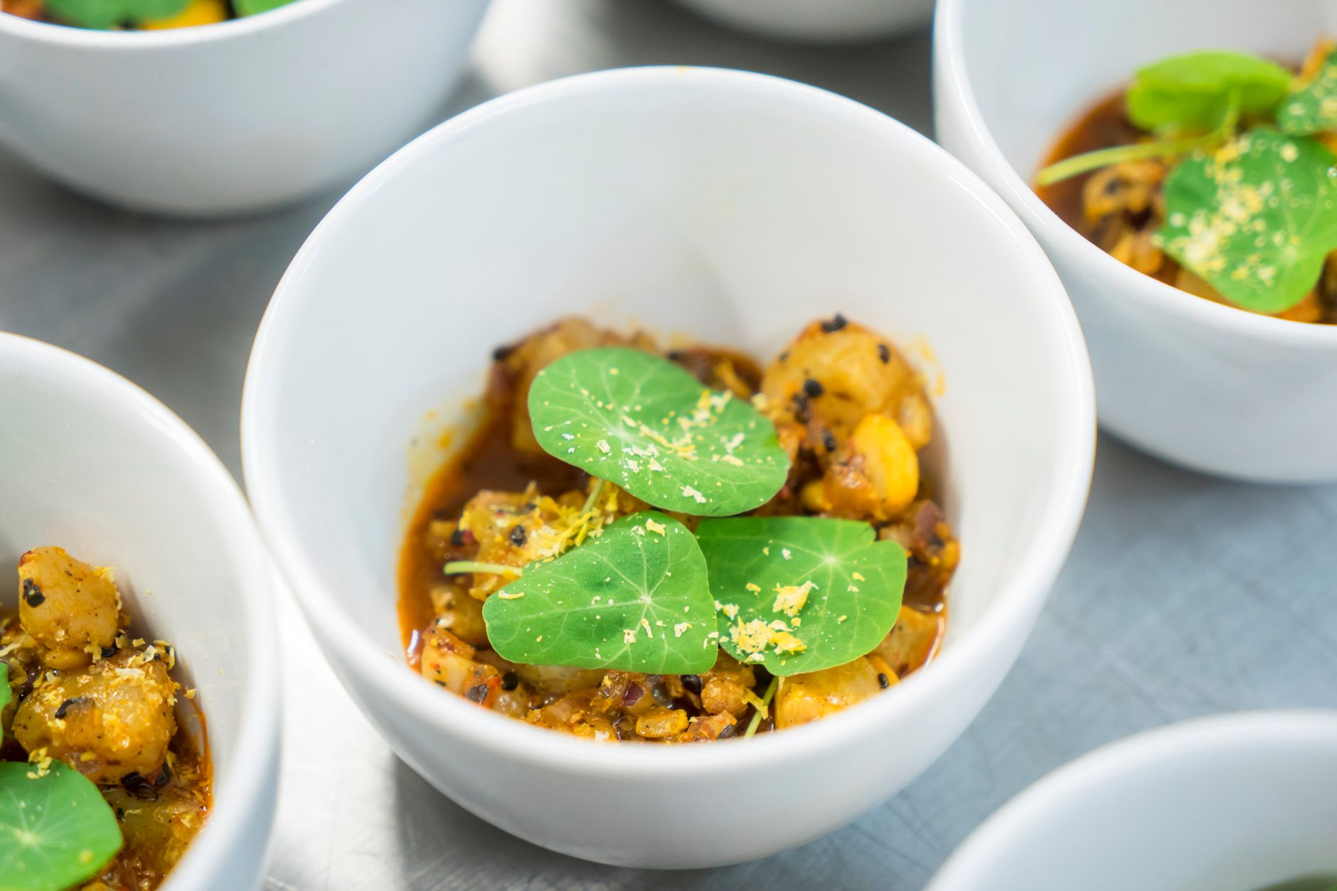 A chef plates a Thai dish at a fine-dining kitchen pass while servers wait nearby.