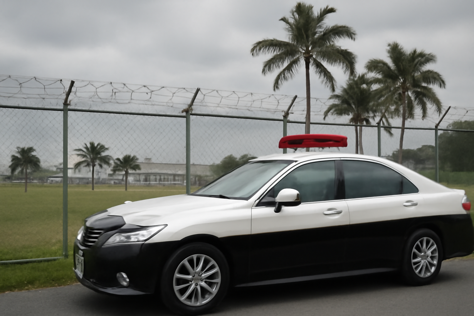 Japanese police vehicle parked near a U.S. military base perimeter fence on Okinawa under overcast sky