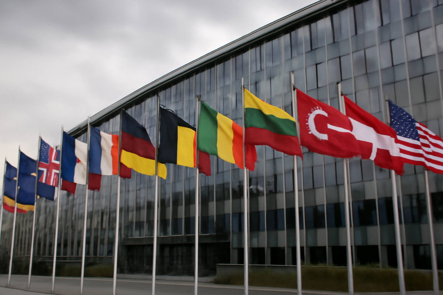 NATO flags lined up outside alliance headquarters under an overcast sky