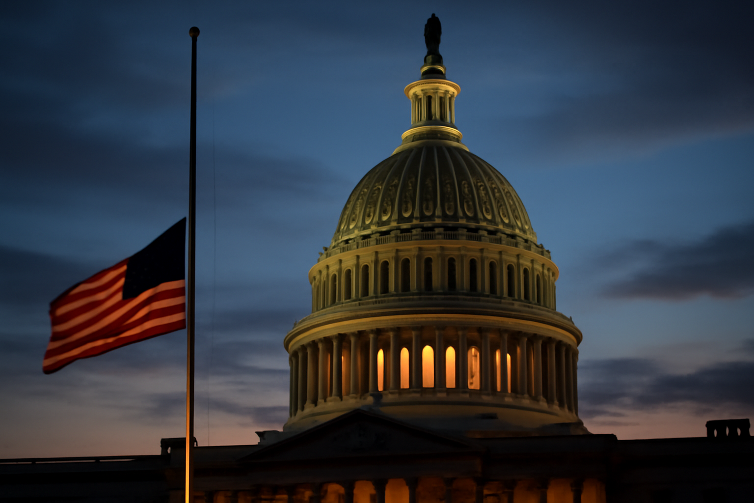 U.S. Capitol dome at dusk with an American flag at half-staff