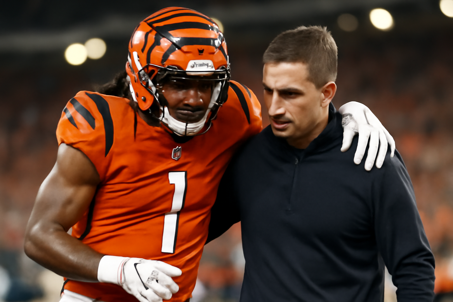 Football player in a Cincinnati Bengals jersey being helped off the field by a trainer