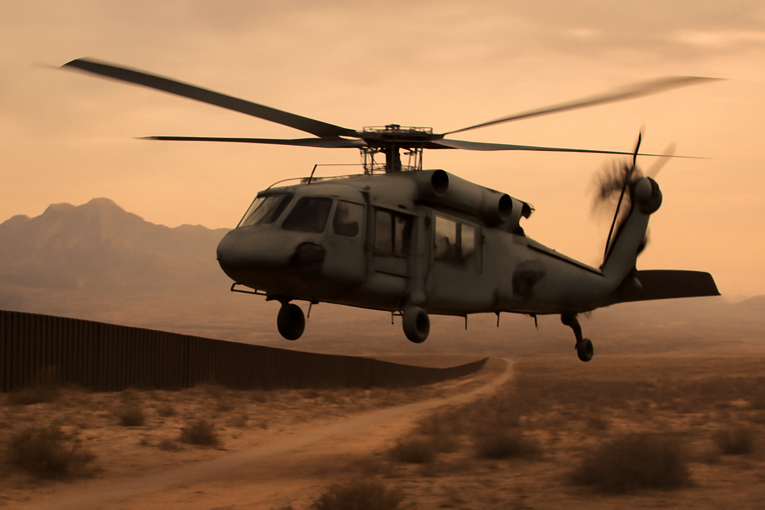 A military helicopter silhouetted against a desert horizon near a mountainous border region at dusk