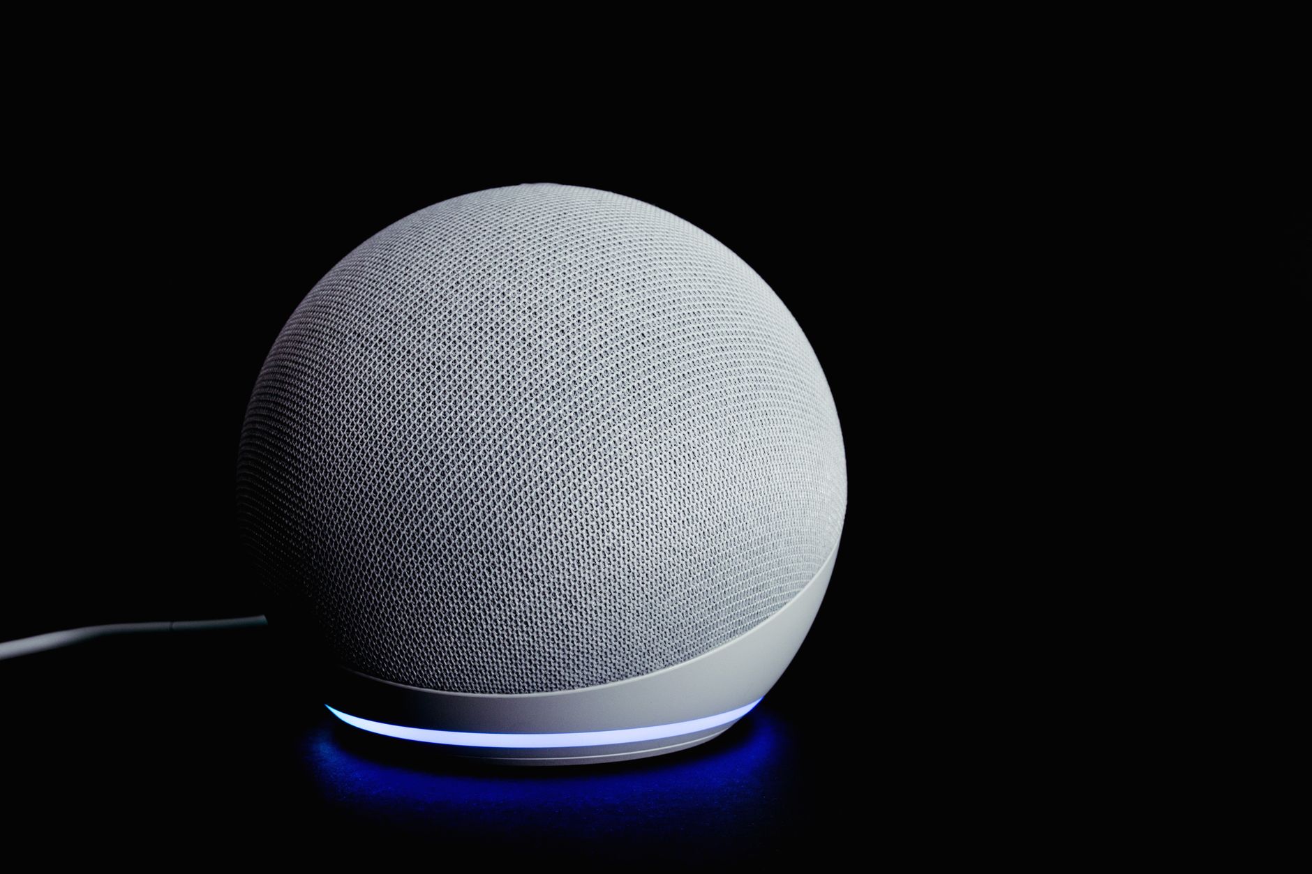 Amazon Echo Dot smart speaker in pastel color next to a bedside clock on a nightstand