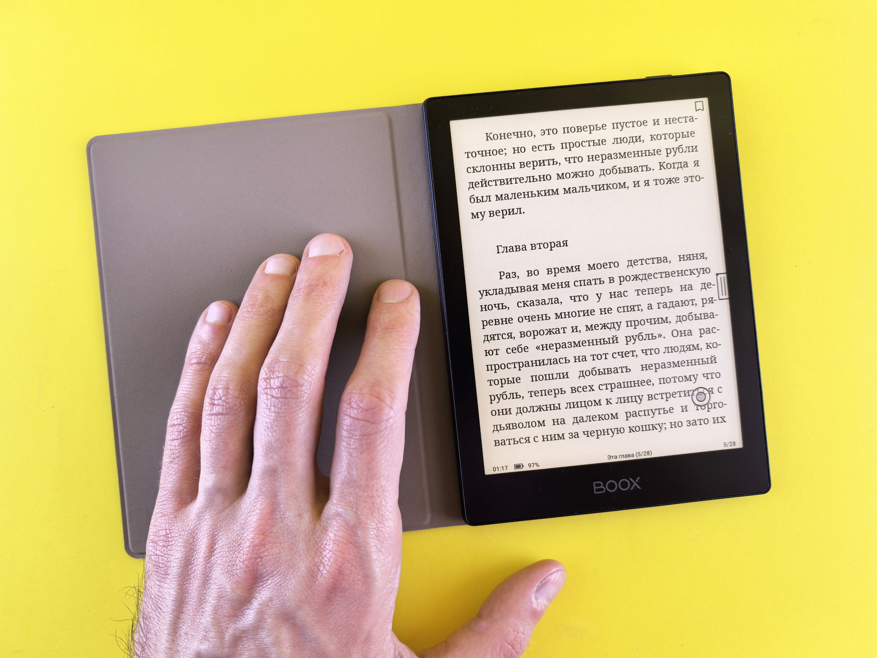 Small E Ink reading tablet with warm-toned screen held in one hand next to a smartphone