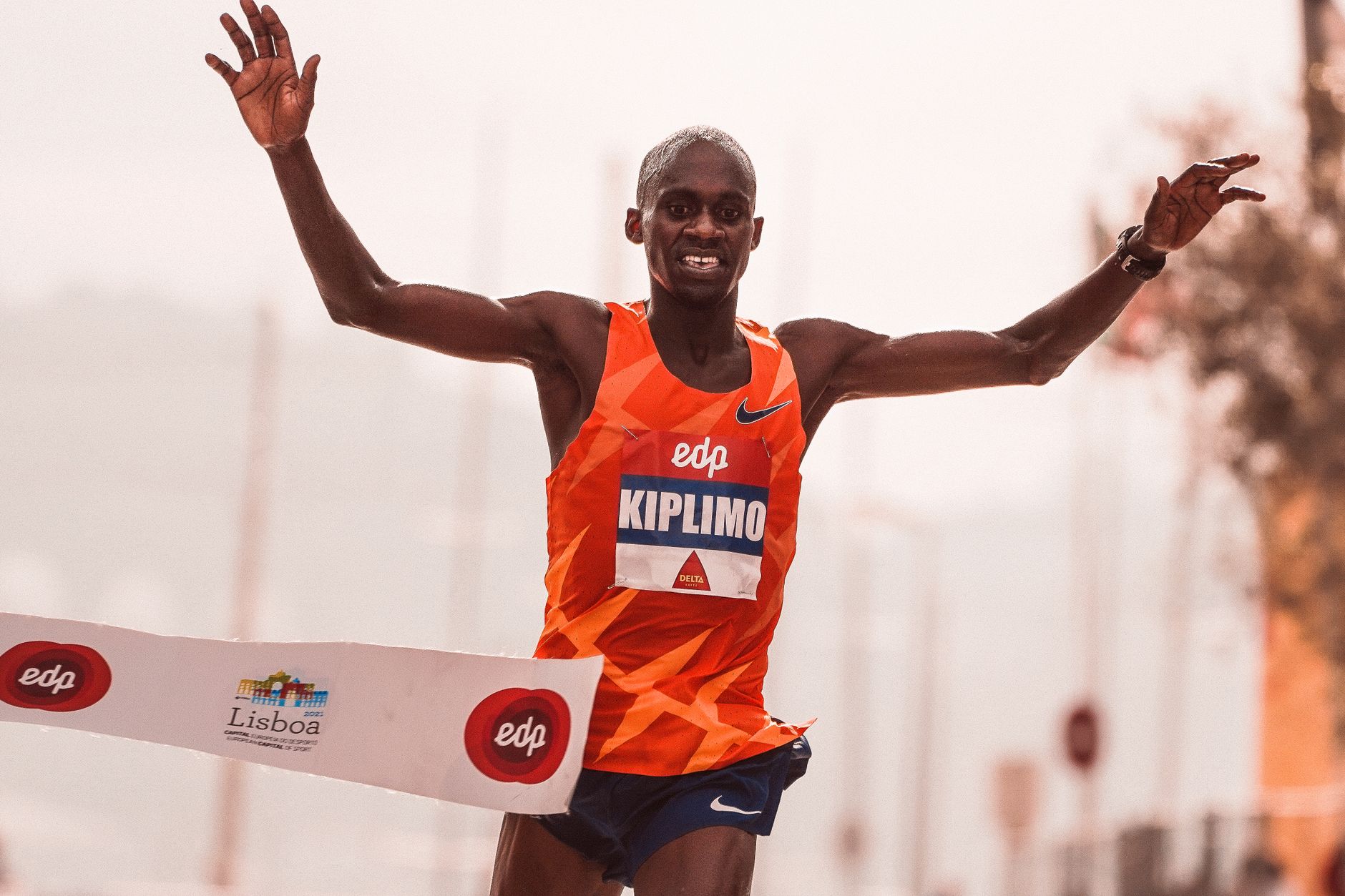 Two elite marathon runners in racing gear facing each other on a city street, one with a raised fist mid rock-paper-scissors gesture