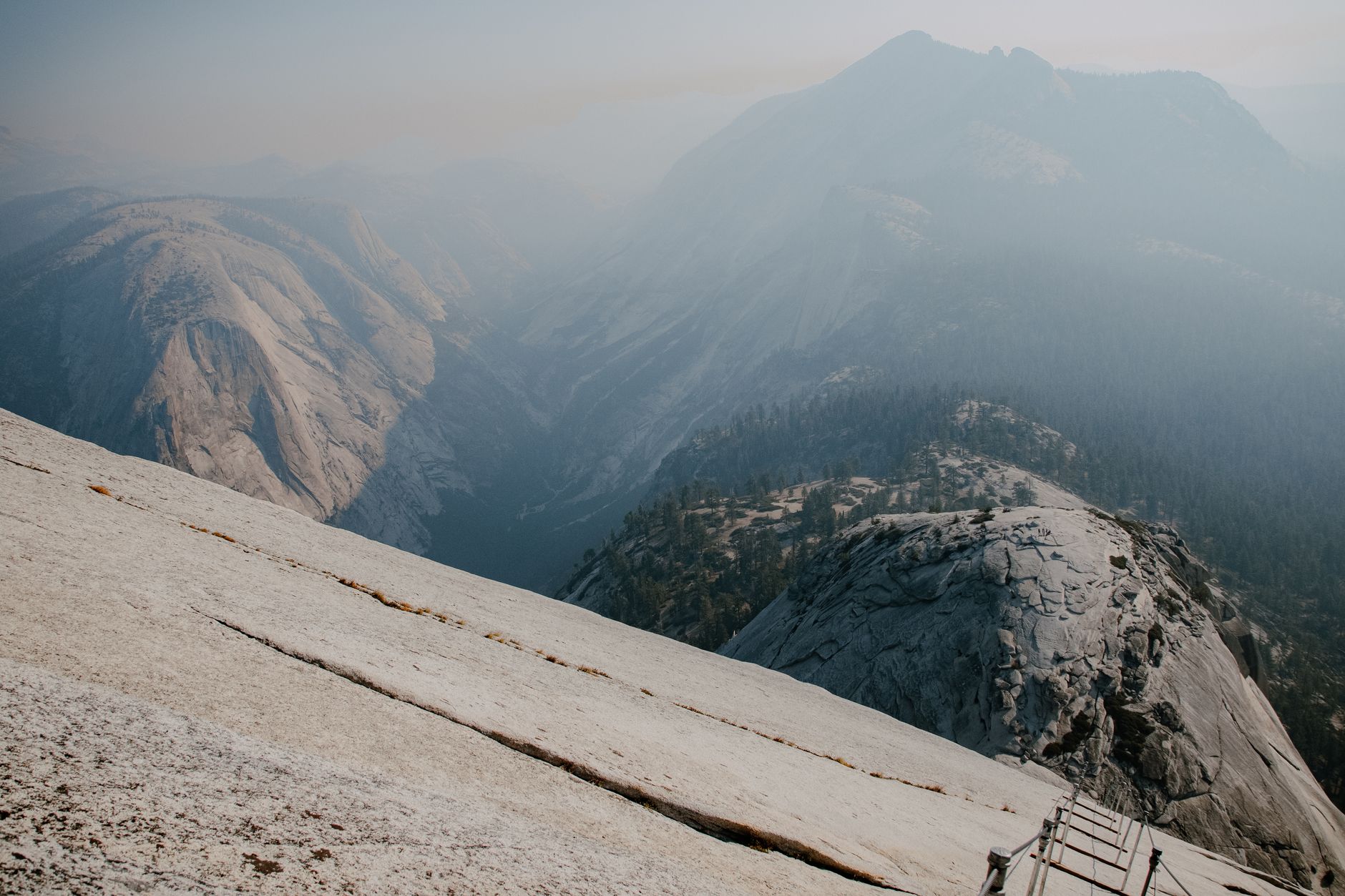 A father and young son roped together on a granite rock face high above a forested valley
