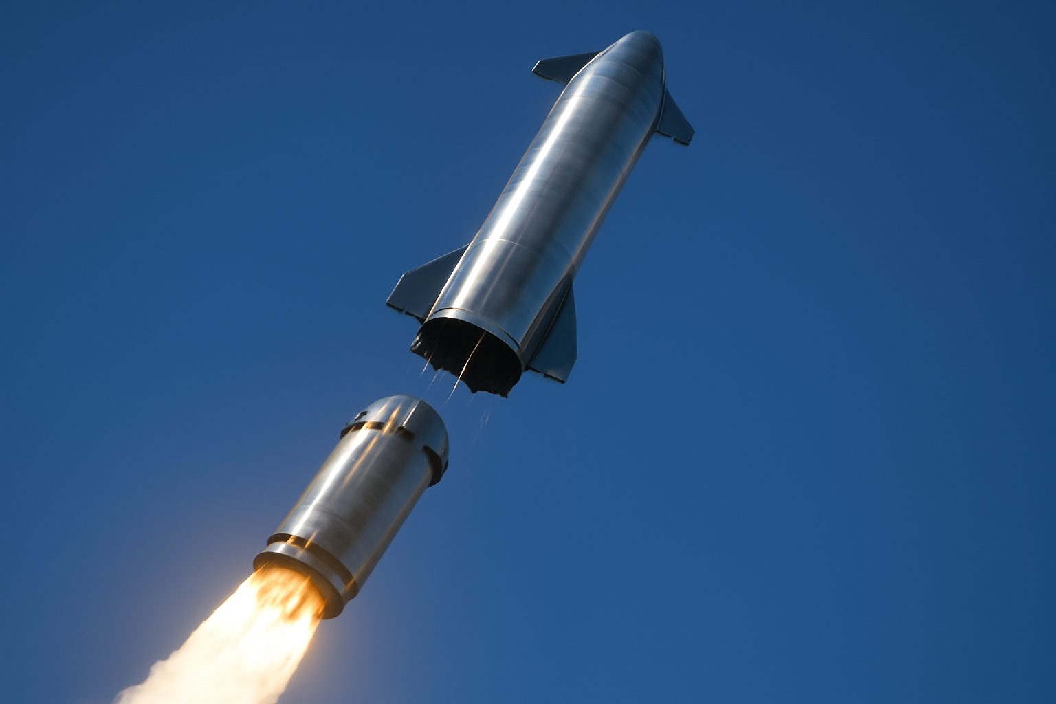 A Starship rocket separating from its booster against a clear sky during ascent