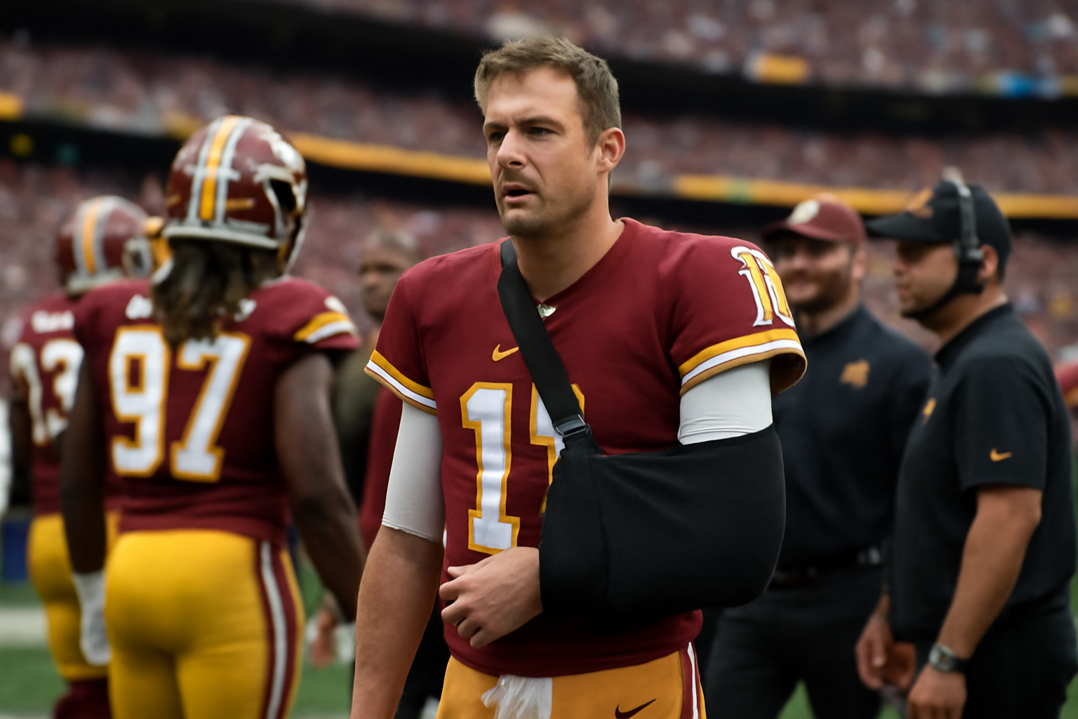 Football quarterback in Washington Commanders uniform standing on sideline with arm in a protective sling