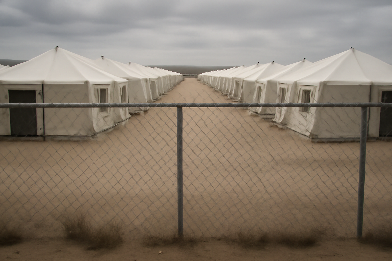 Rows of white tents behind a chain-link fence at a desert detention camp in west Texas