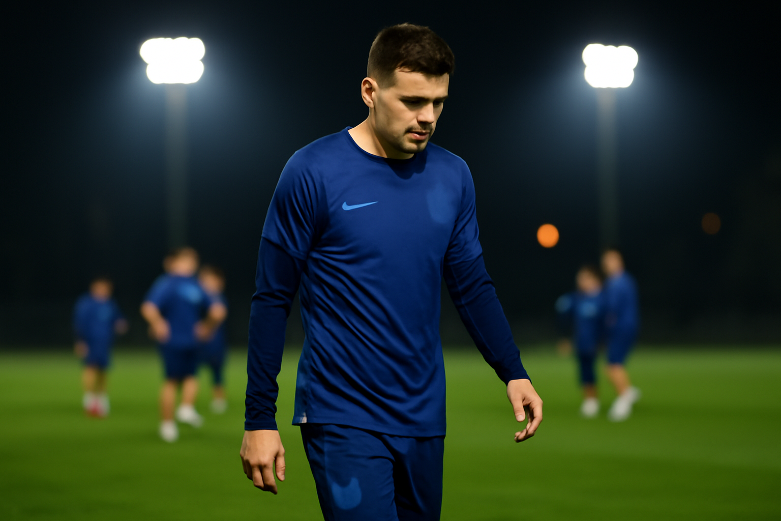 Soccer player in national team uniform walking off a training pitch alone