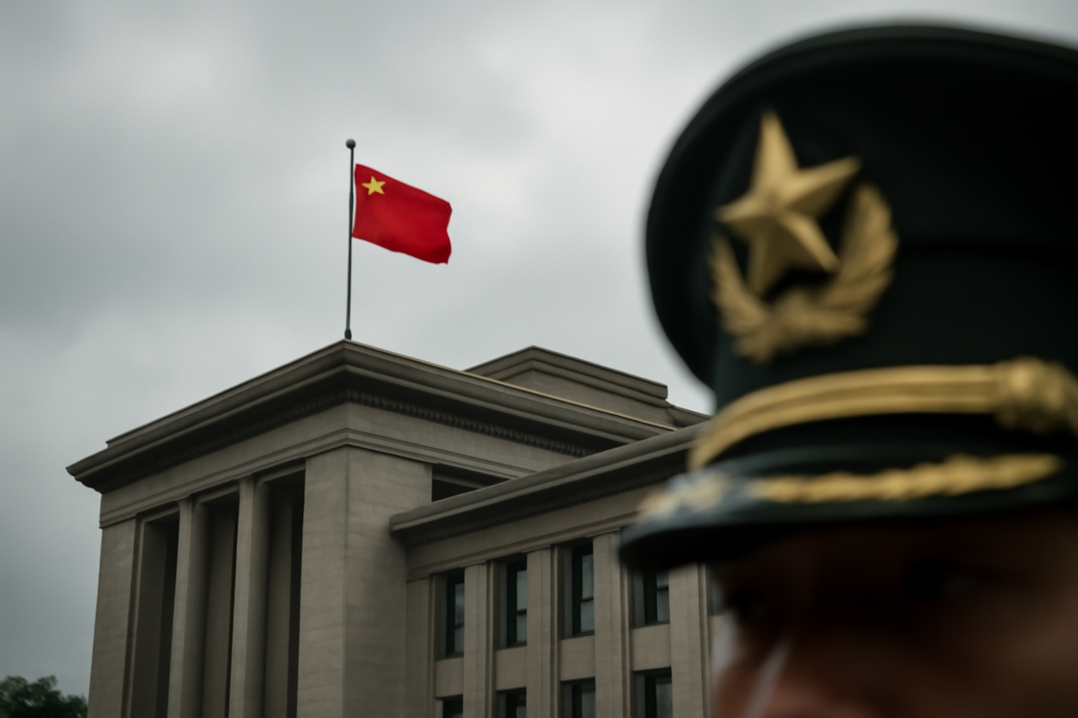 Chinese military insignia and a red party flag photographed against a gray government building facade