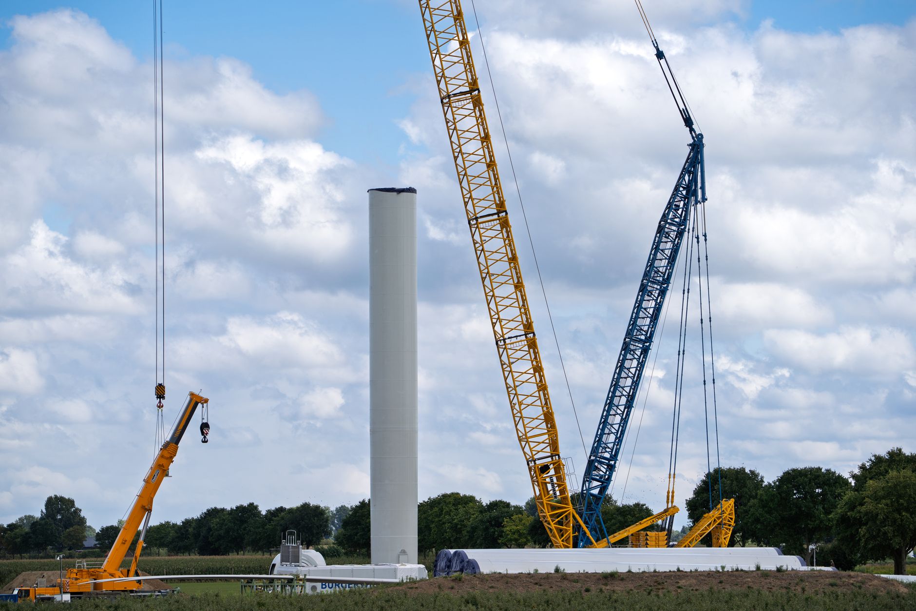 Wind turbines standing in a field under an overcast sky near transmission lines