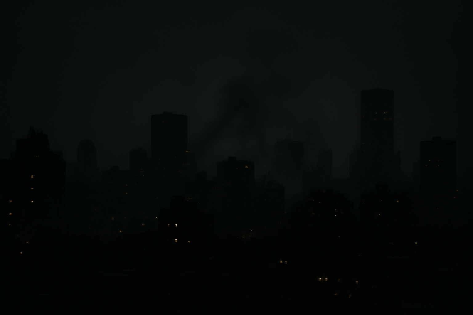 Smoke rising over a city skyline at night with silhouettes of buildings in the foreground