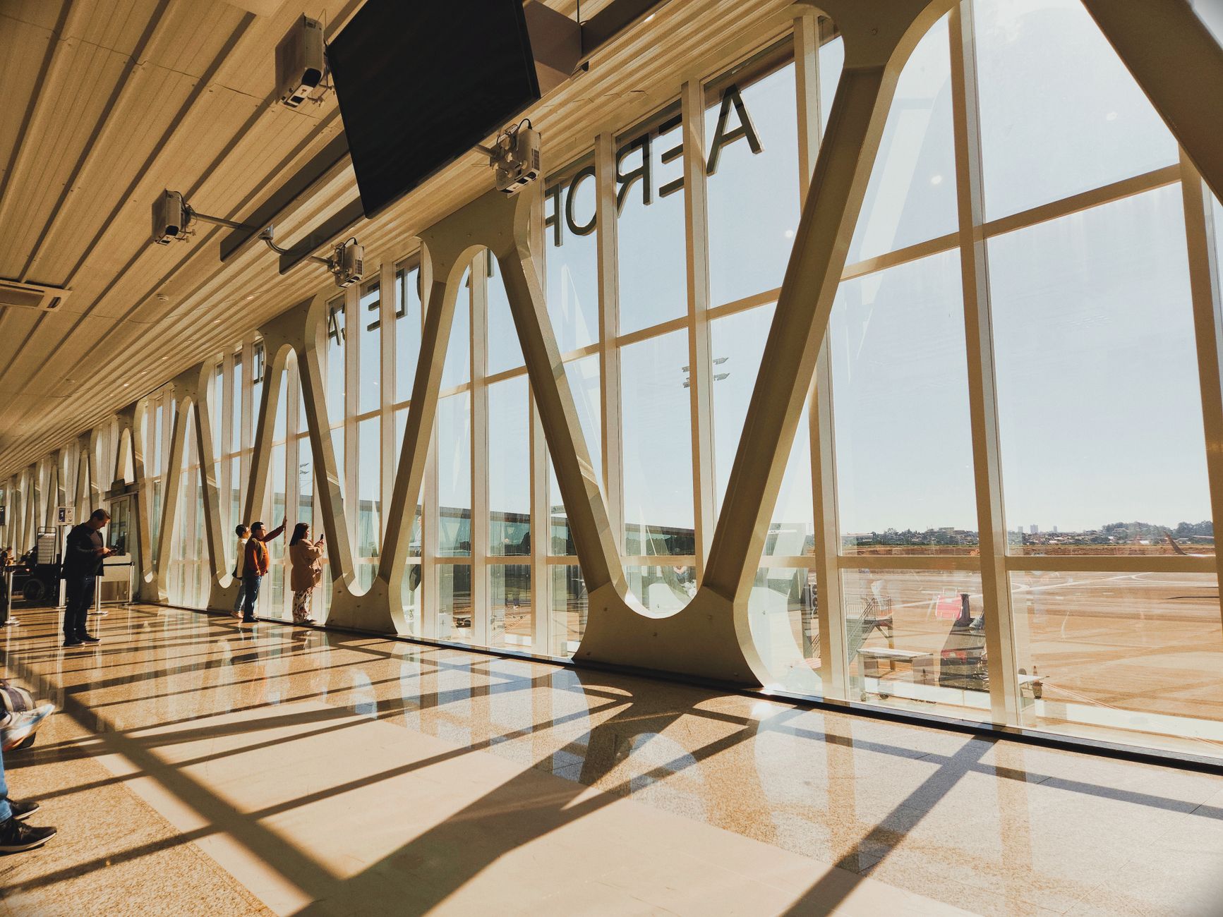 Travelers with luggage moving through a bright, newly opened airport terminal with large glass windows