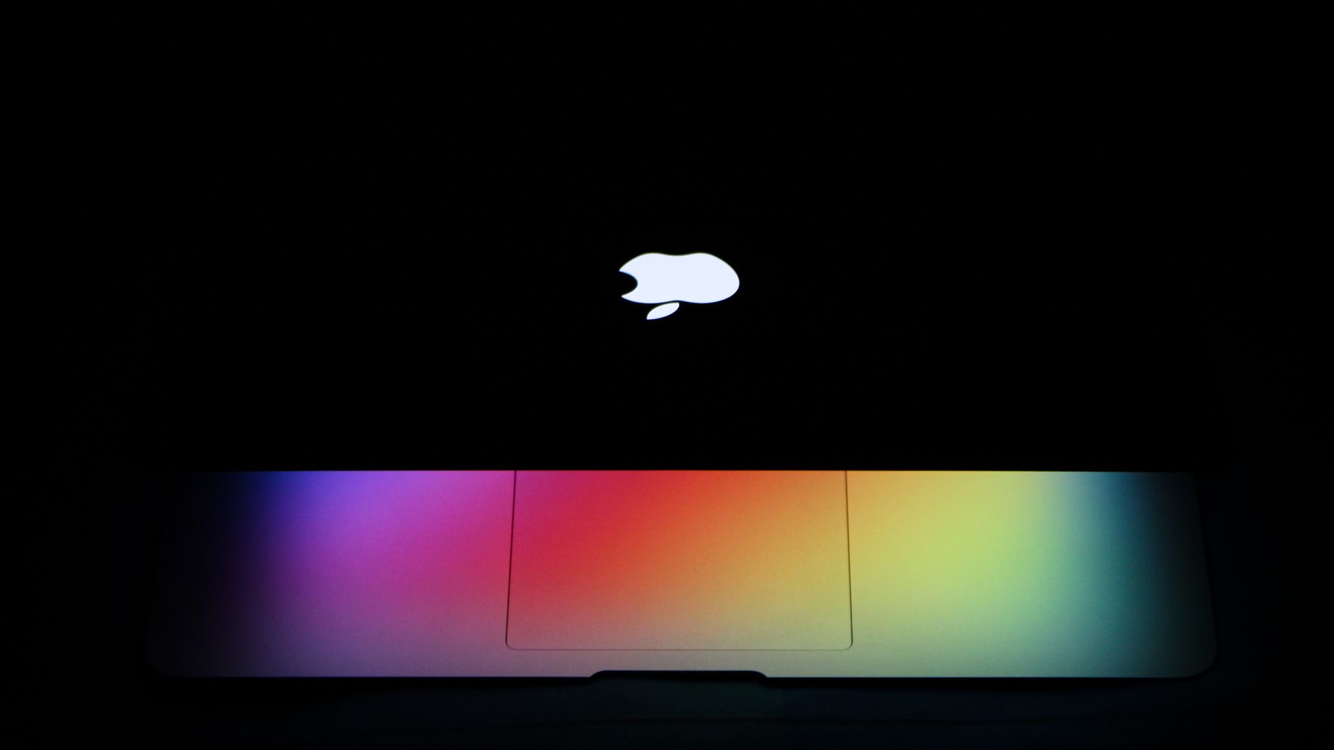 Silver MacBook Pro laptop open on a desk showing a dark wallpaper and Apple logo