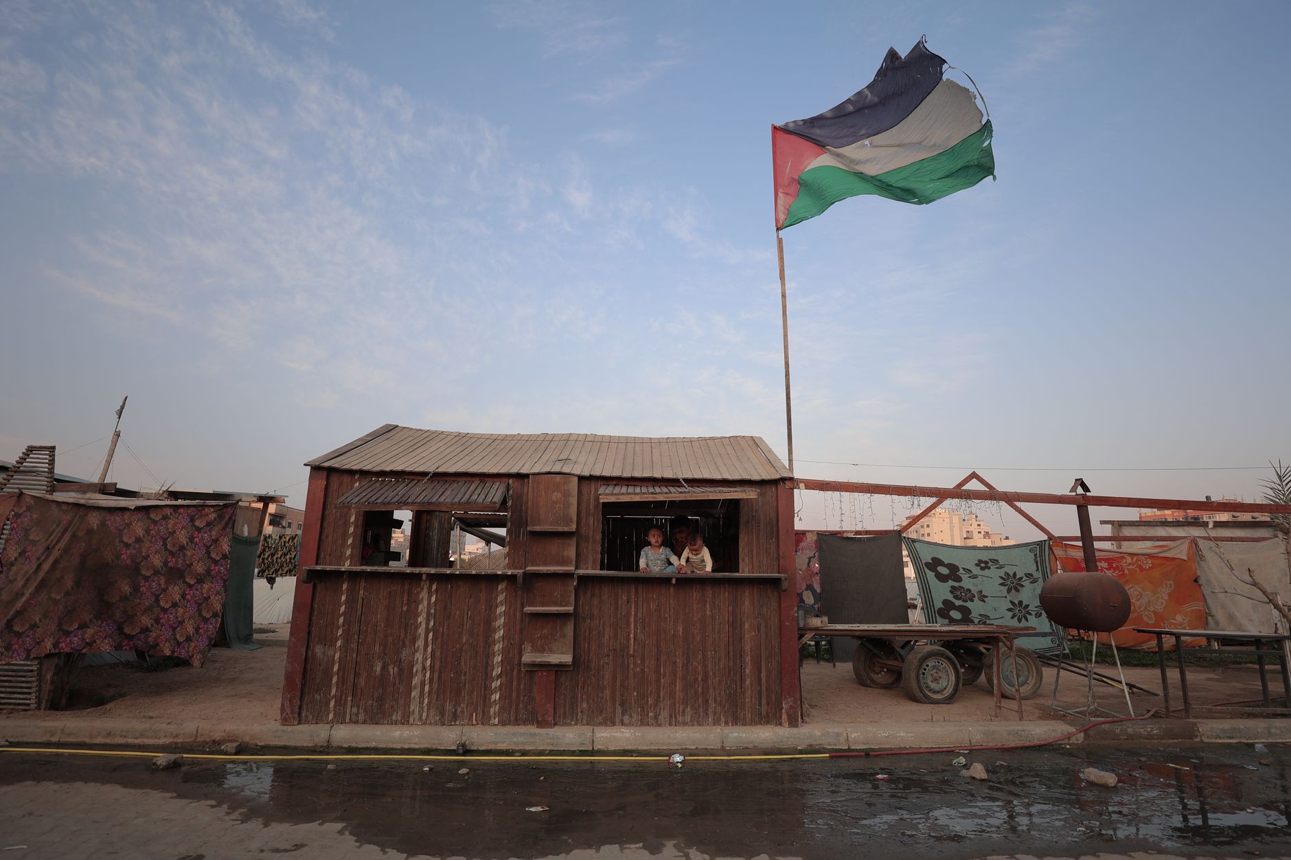 A metal gate across a dirt road near a West Bank hillside town at dawn
