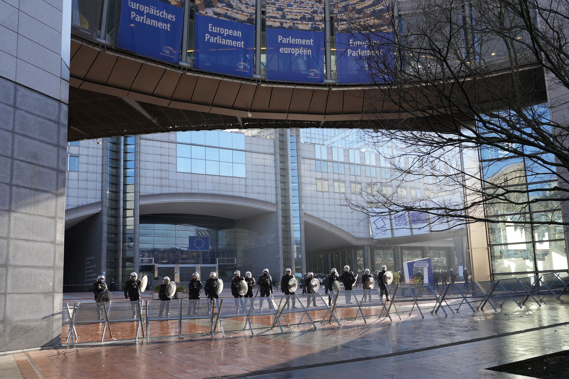 Riot police stand in formation near marching protesters holding union banners on a city street in Italy