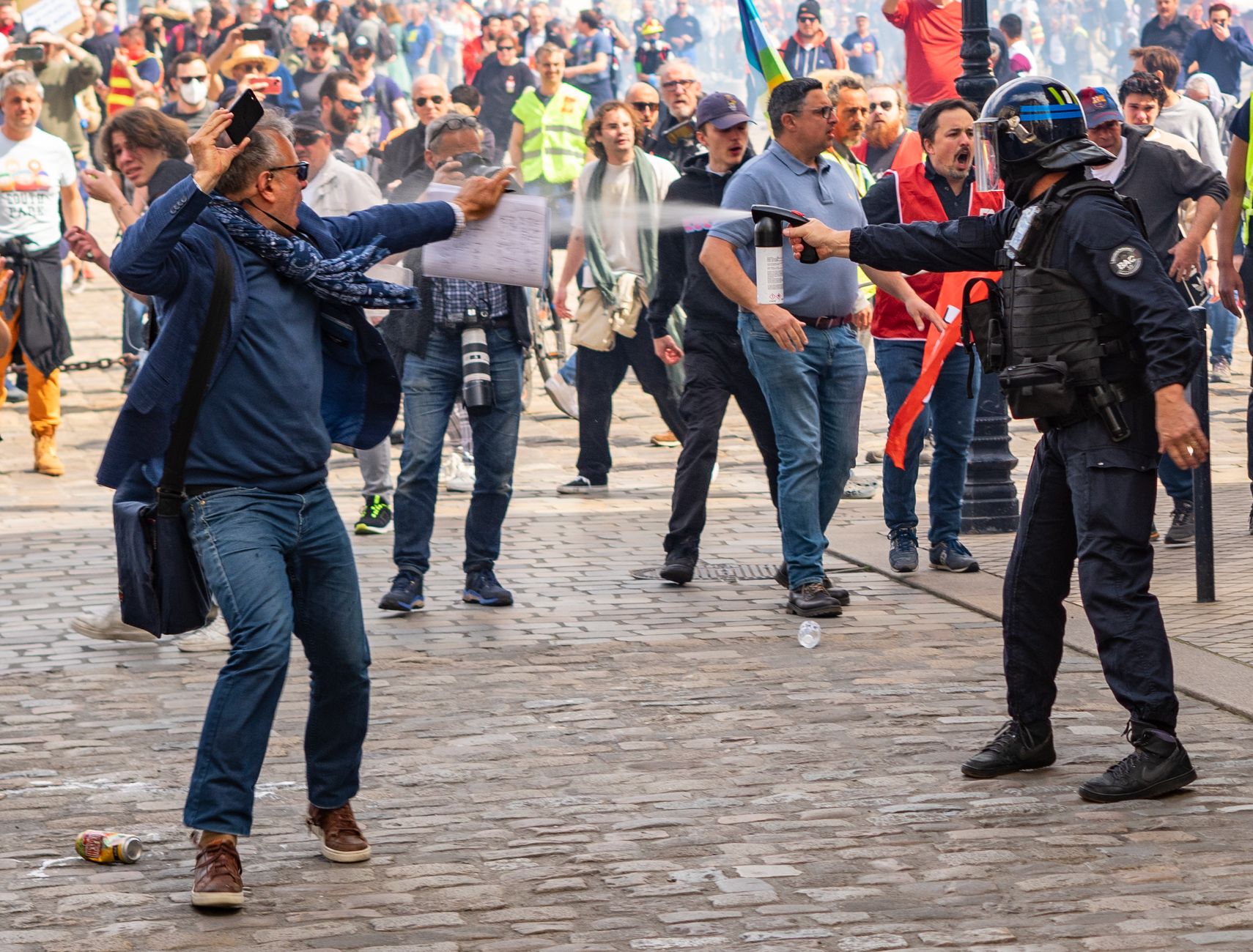 Riot police forming a line on a French city street as a crowd of demonstrators gathers nearby